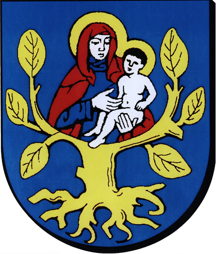 Obrazek przedstawia herb Gminy Olszówka, na którym na ciemnoniebieskim tle znajduje się złote drzewo. Na drzewie widzimy Matkę Boską w czerwono-granatowej szacie, trzymającą na kolanach nagie dzieciątko Jezus.